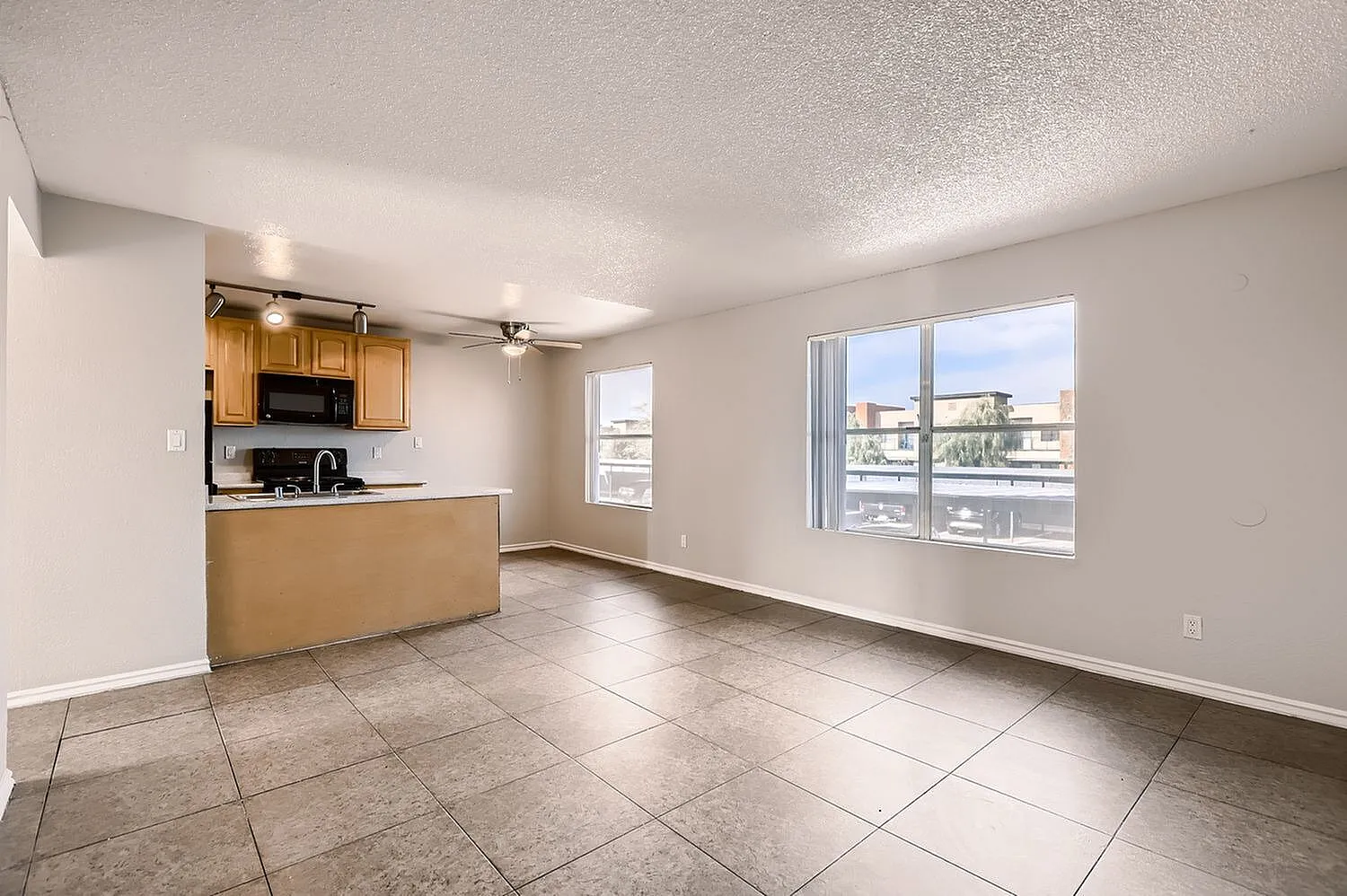 Kitchen with wood cabinetry and black appliances, open living area with wood-style plank flooring, large windows with city views