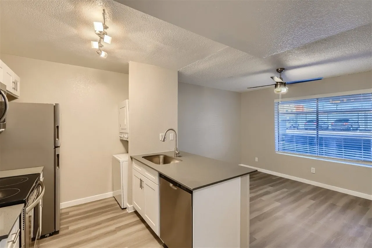 Kitchen, white cabinetry, stainless steel sink, wood-style plank flooring, living area with windows