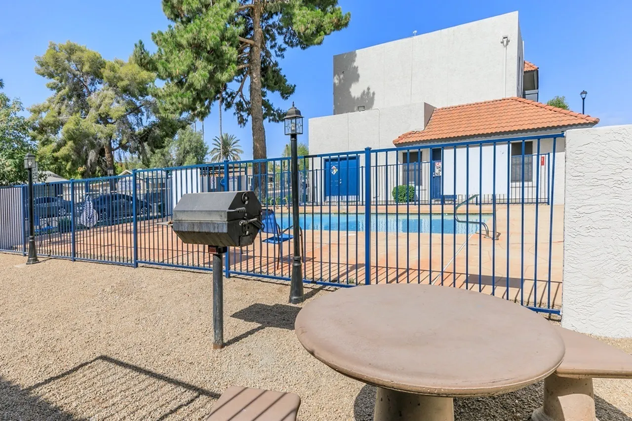Community courtyard with blue metal fencing, round table, grill, mature trees