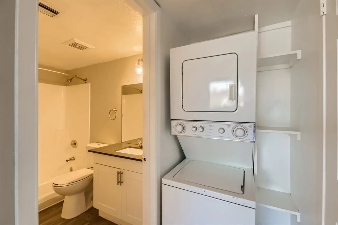 Laundry room with stacked washer and dryer, white cabinetry, bathroom with vanity mirror and toilet