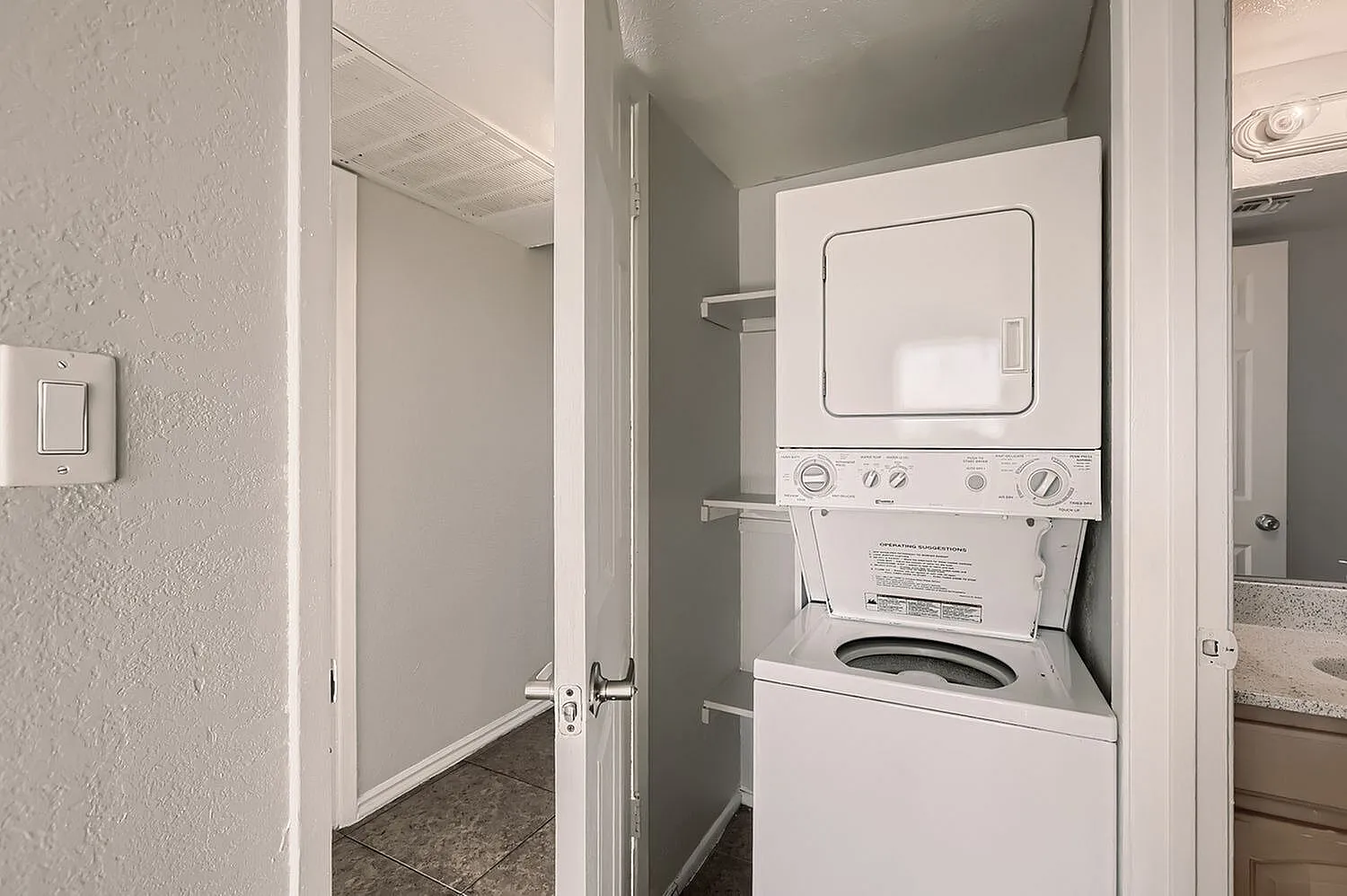 Laundry closet, stacked white washer and dryer, built-in shelving, ceramic tile flooring