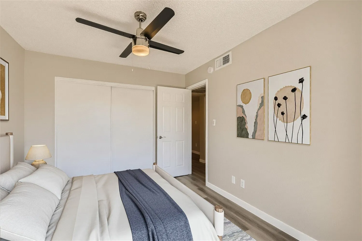 Primary bedroom, wood-style plank flooring, ceiling fan with light, wall art