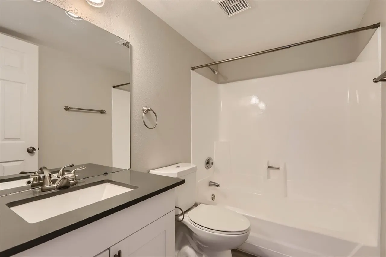 Bathroom, single vanity with dark countertop, white ceramic sink, glass shower enclosure, white tile surround