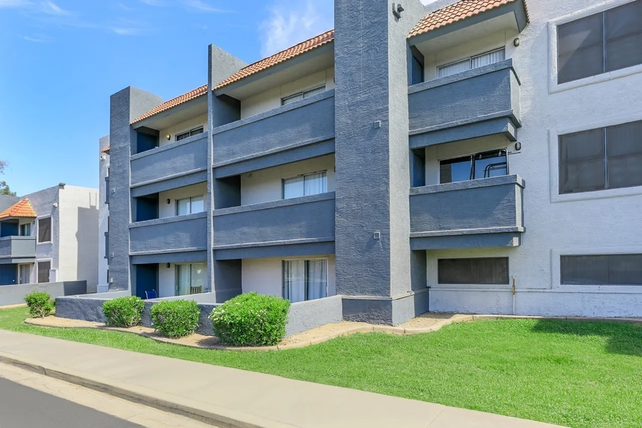 Modern apartment building, glass balcony railings, landscaped lawn, blue sky