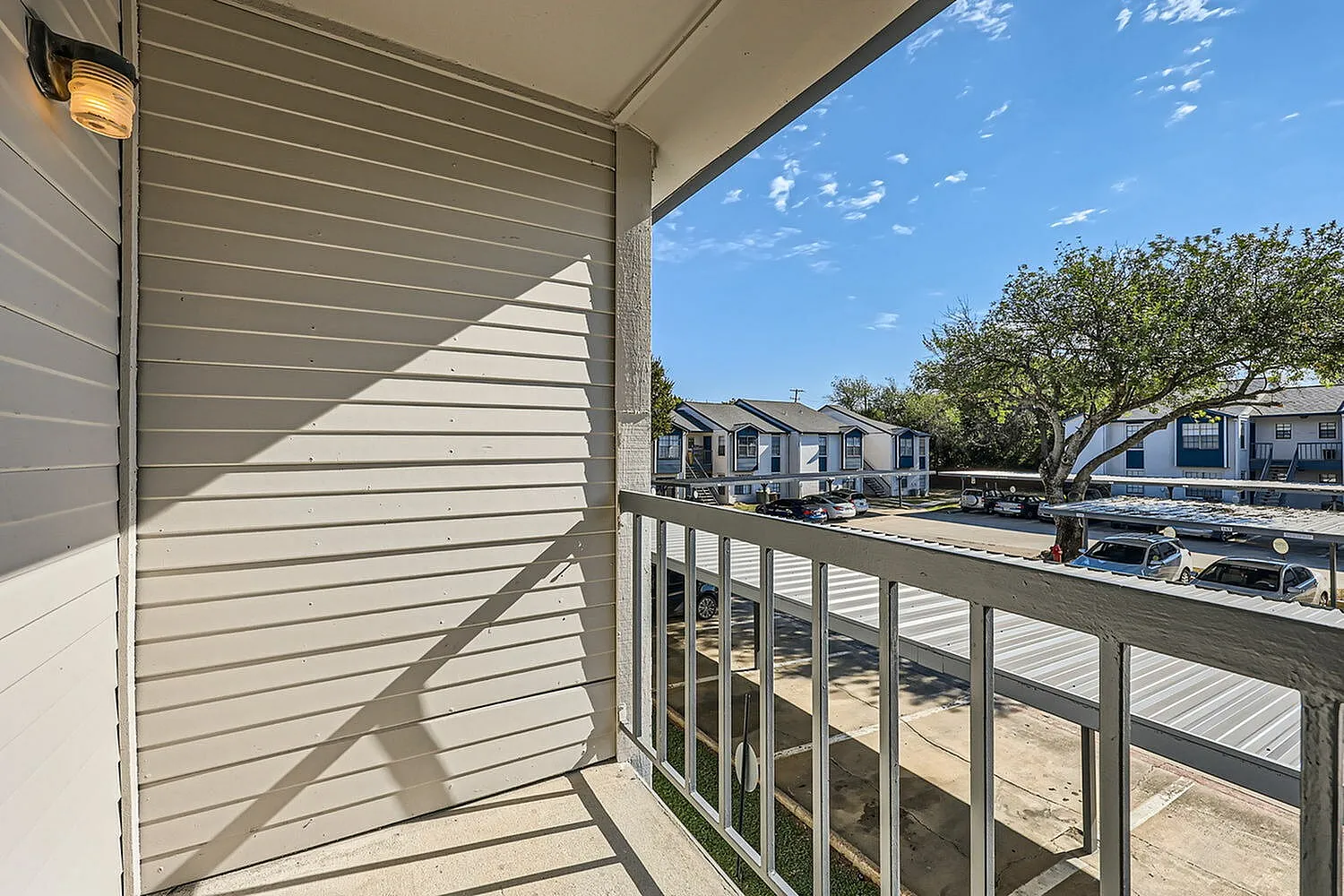 Balcony, gray metal railing, siding wall, community buildings and trees