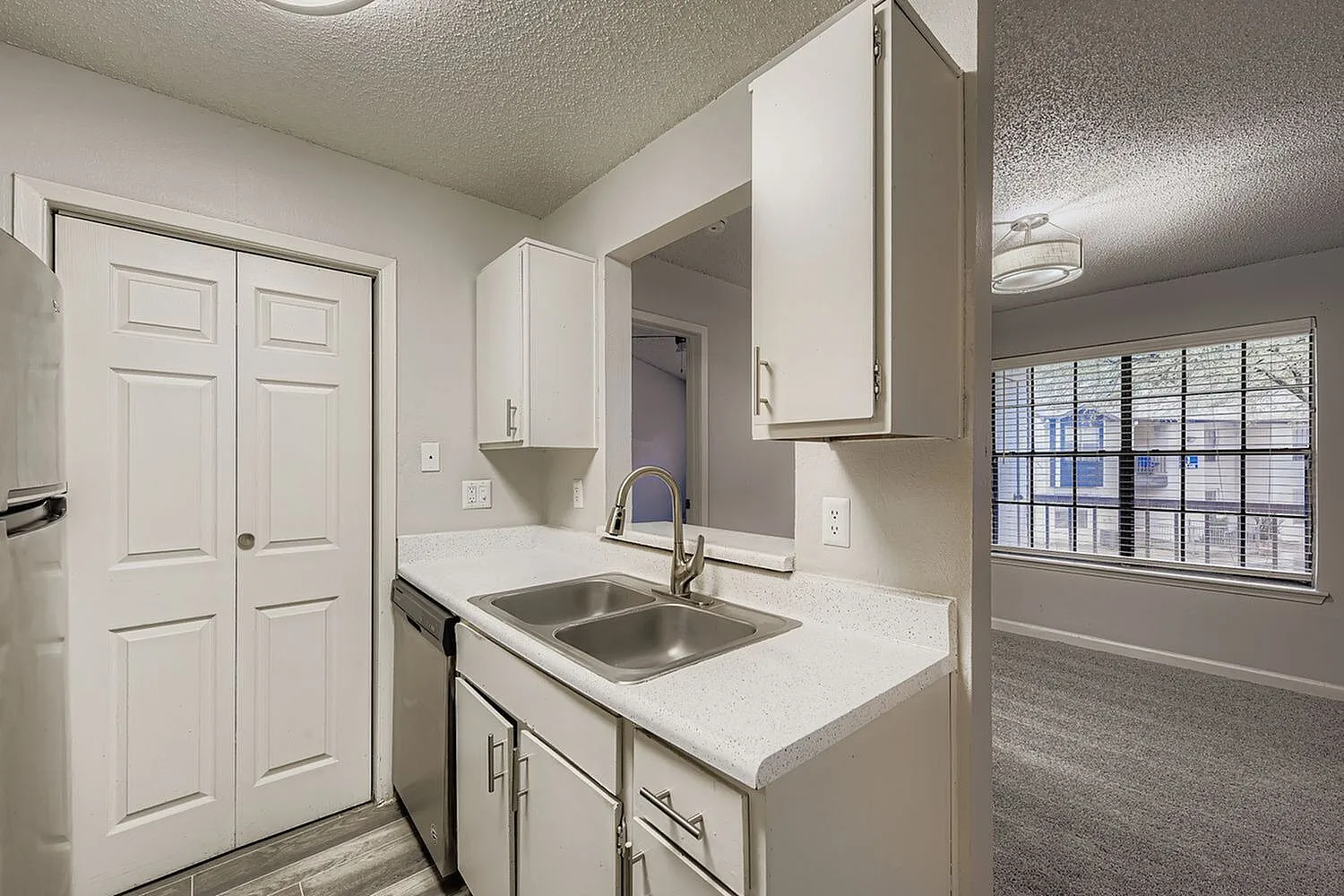 Kitchen with white cabinetry, quartz countertops, stainless sink, white appliances, bathroom vanity visible, wood-style plank flooring
