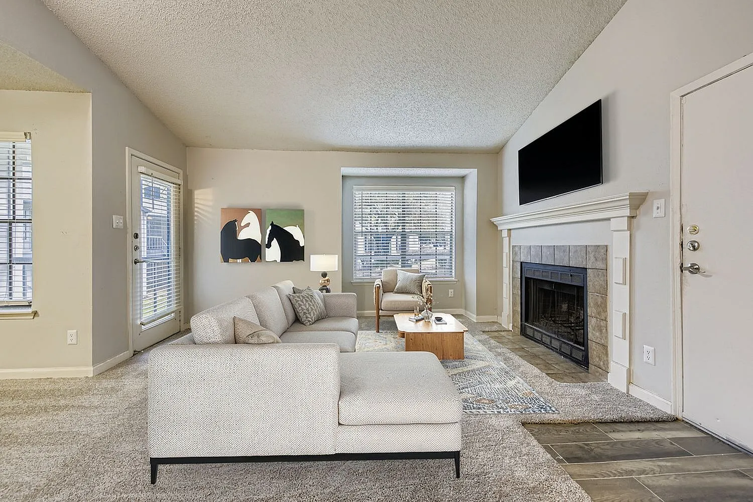 Living room with wood-style plank flooring, fireplace with white mantel, flat-screen TV, neutral sectional sofa