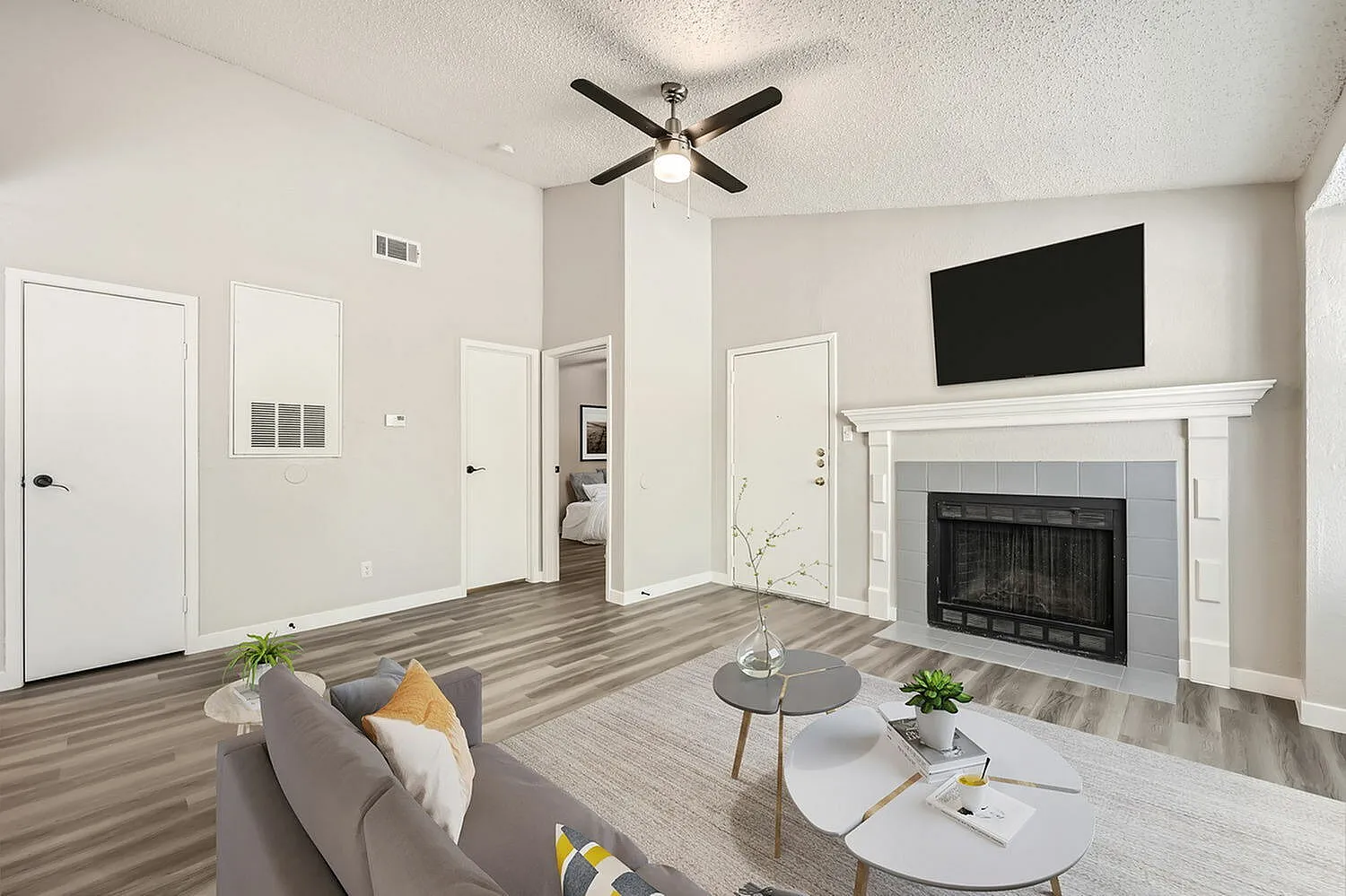 Living room with wood-style plank flooring, fireplace with white mantel, ceiling fan, wall-mounted TV