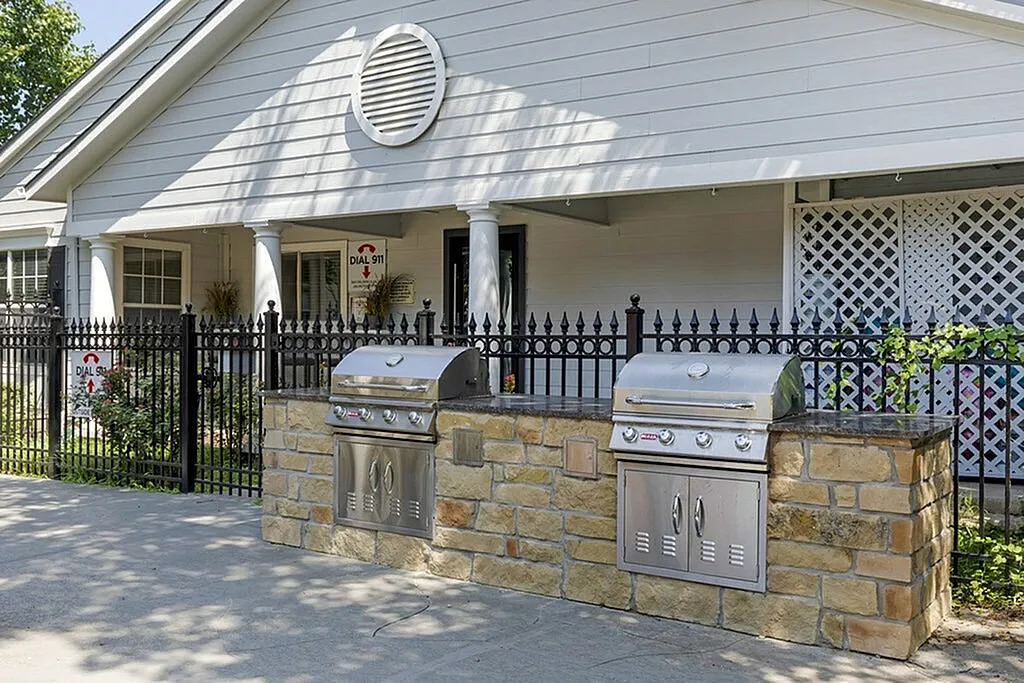 Outdoor kitchen with stainless steel grills, stone countertops, white columns, black metal fence