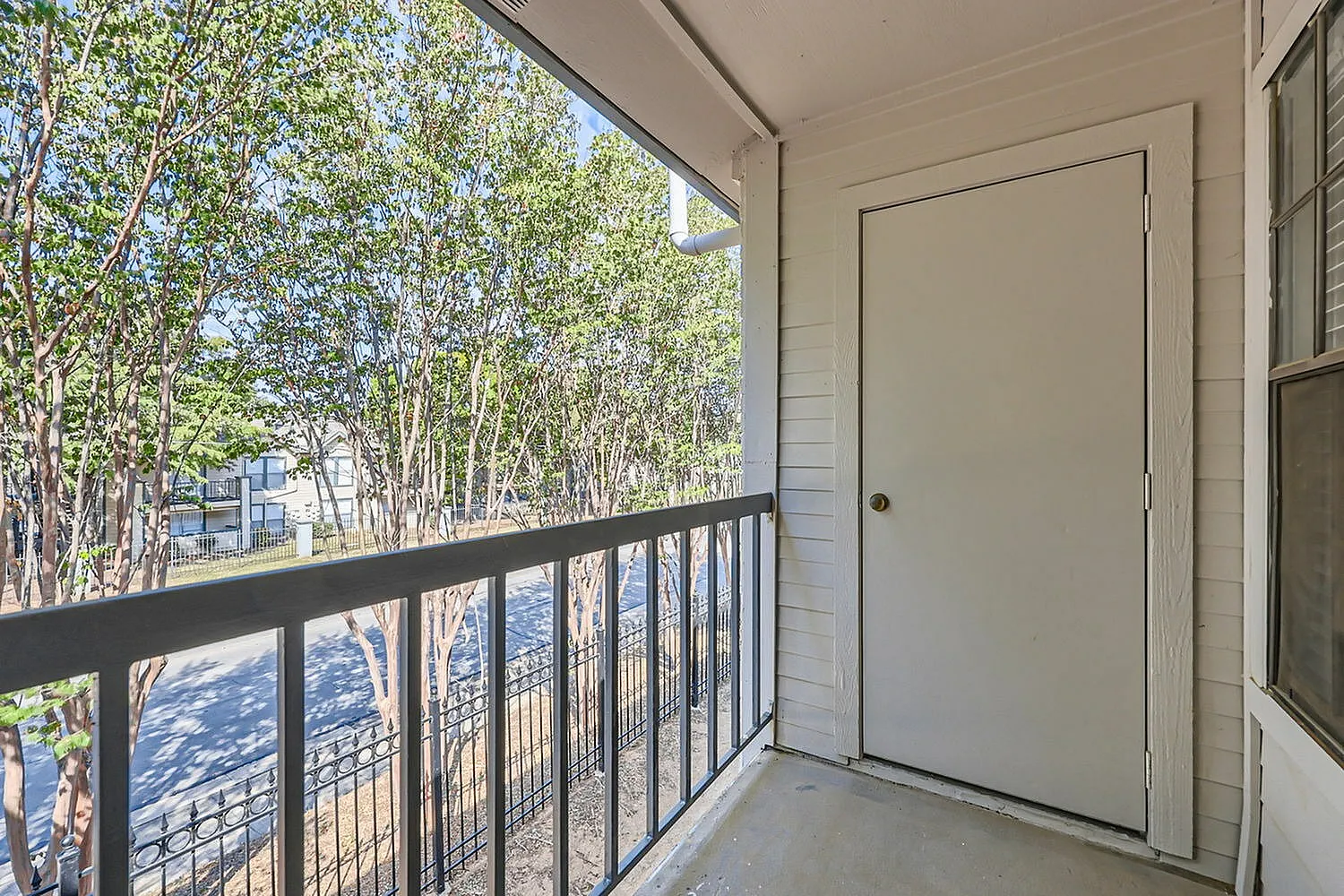 Balcony, metal railing, concrete flooring, white door, tree views