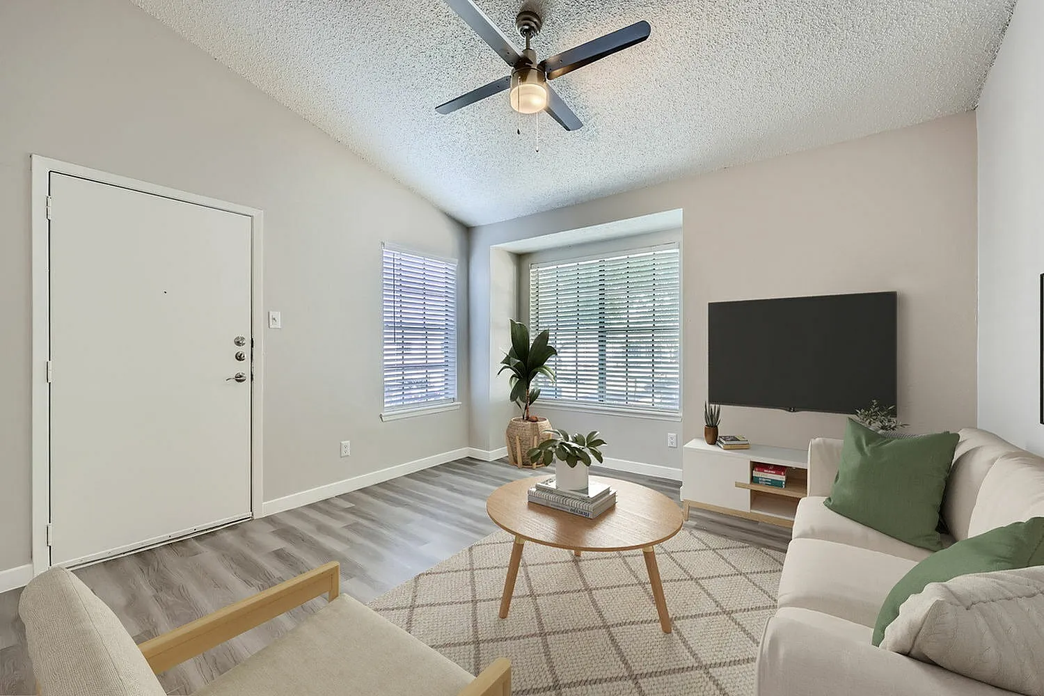 Living room with wood-style plank flooring, ceiling fan, flat-screen TV, entry door