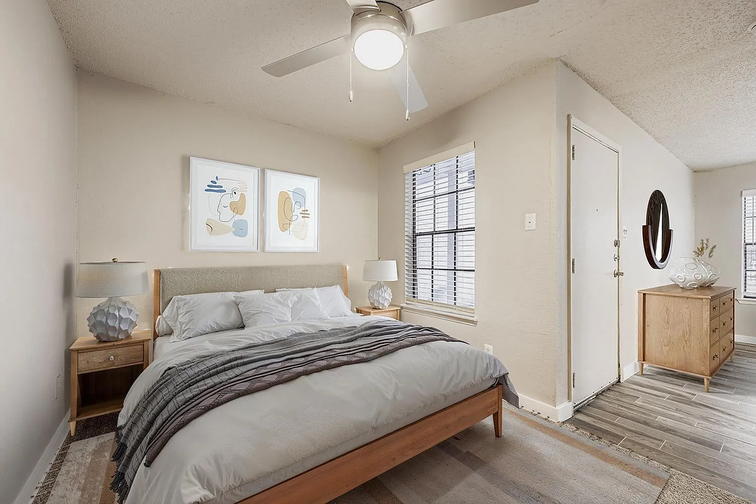 Primary bedroom, wood-style plank flooring, ceiling fan, upholstered headboard, wood nightstands, ensuite bathroom visible