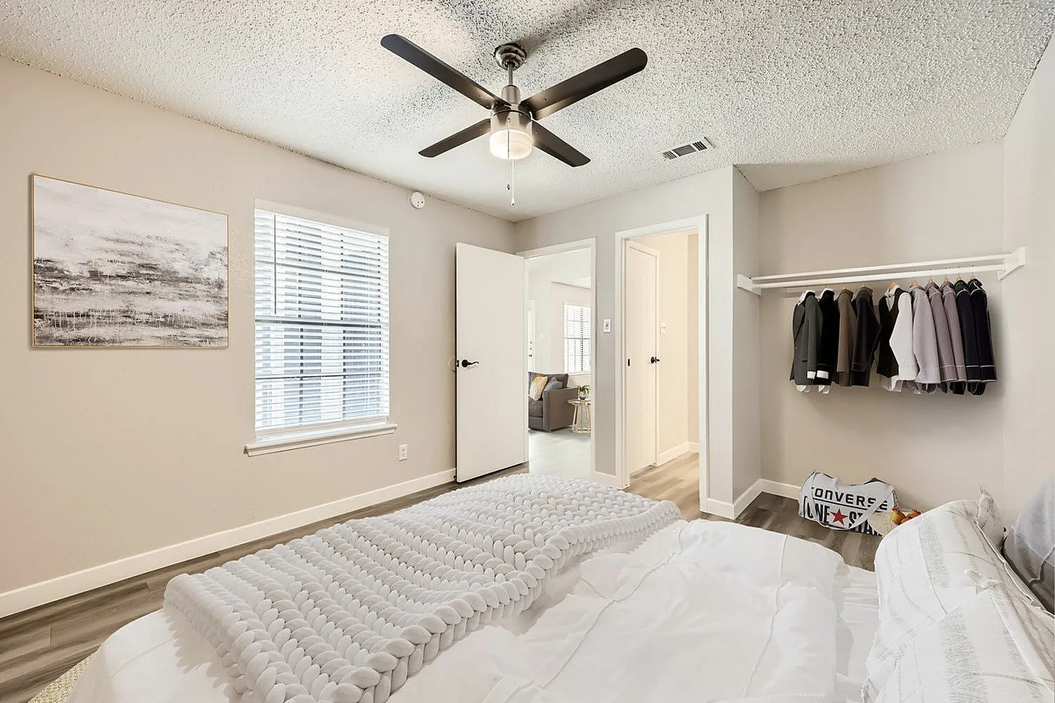 Primary bedroom, wood-style plank flooring, ceiling fan, window with shutters, clothing rod