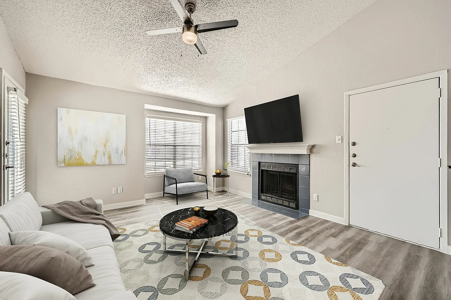 Living room, wood-style plank flooring, ceiling fan, fireplace with TV, entry door