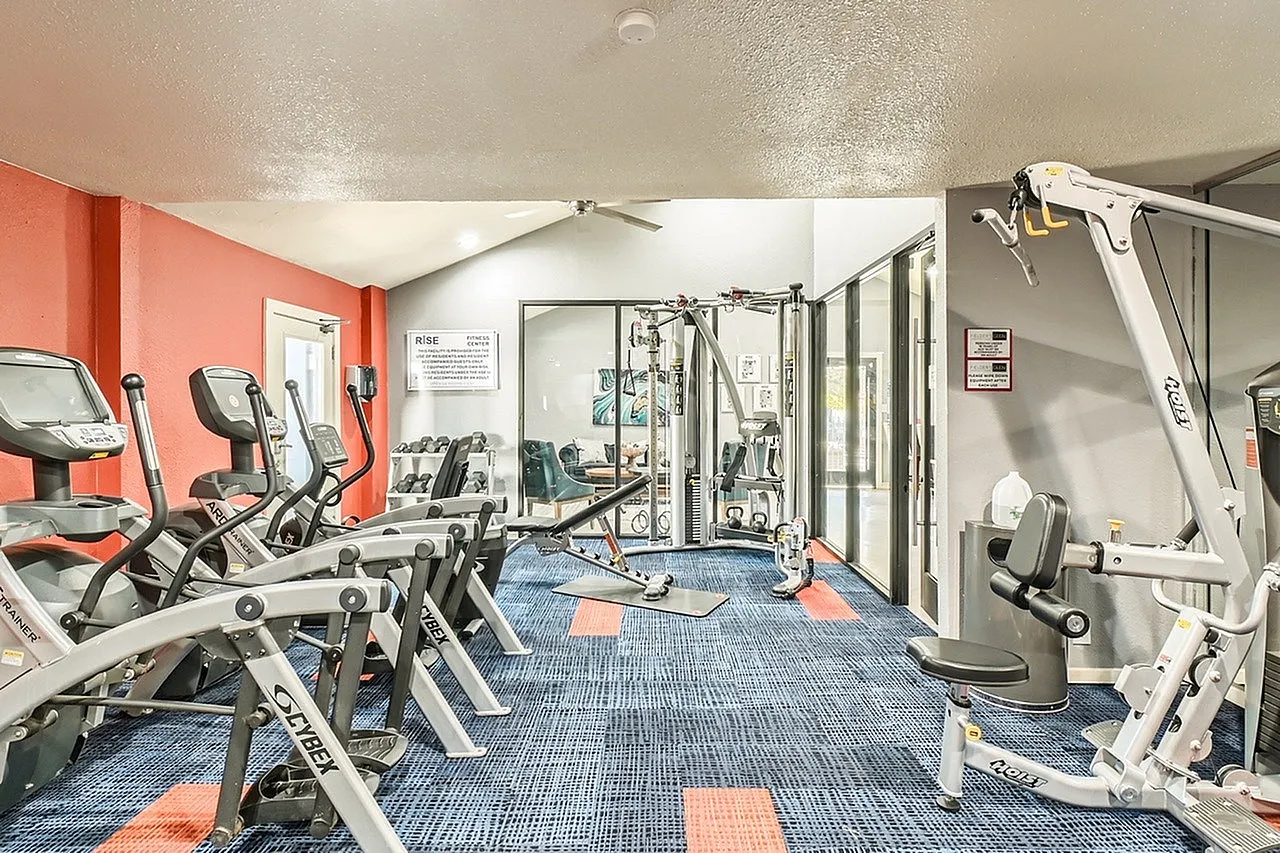 Fitness center, exercise equipment, blue and orange patterned flooring, red accent wall, mirrored gym space