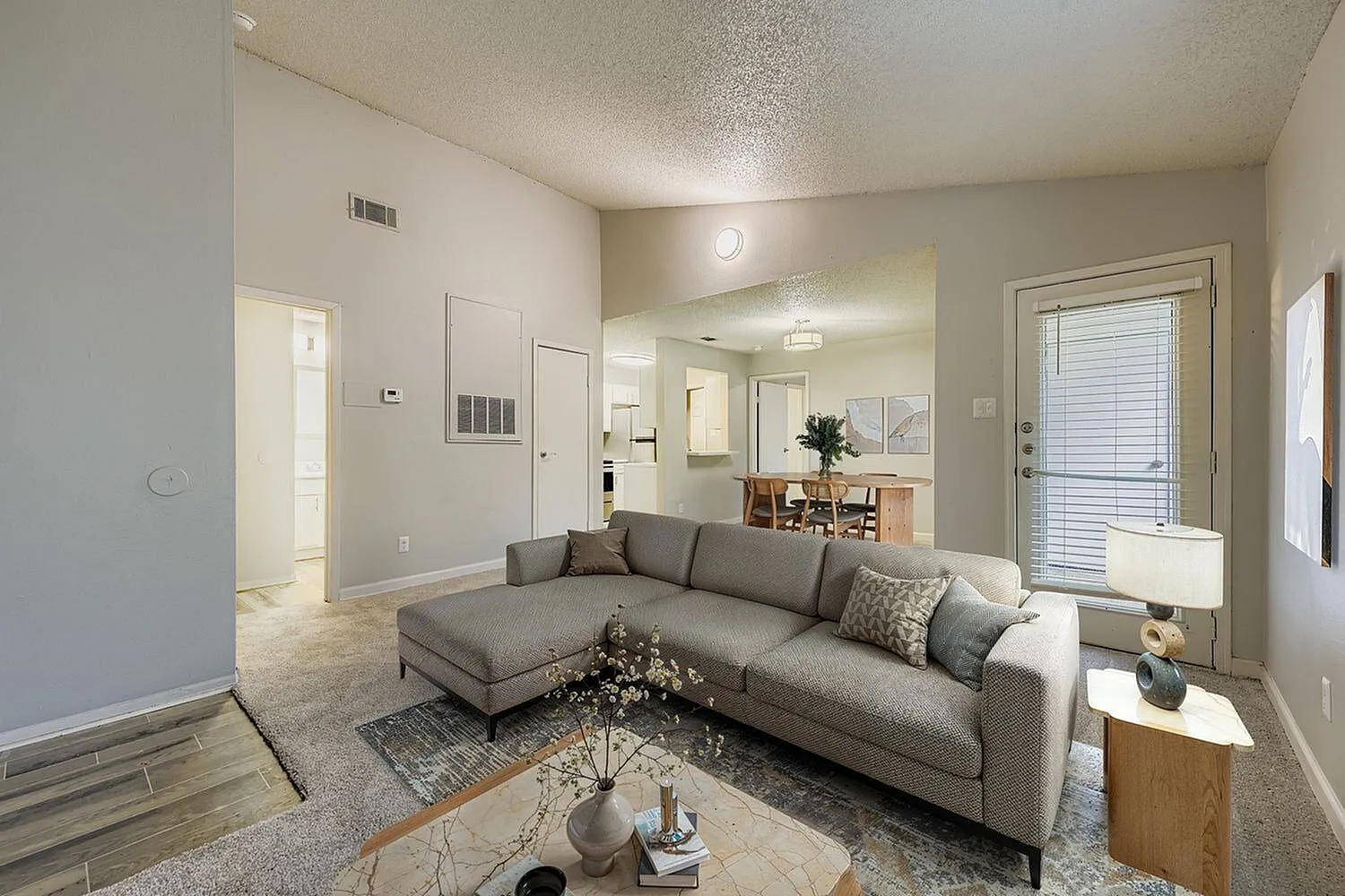 Living room, gray sectional sofa, wood-style plank flooring, open kitchen view, contemporary decor