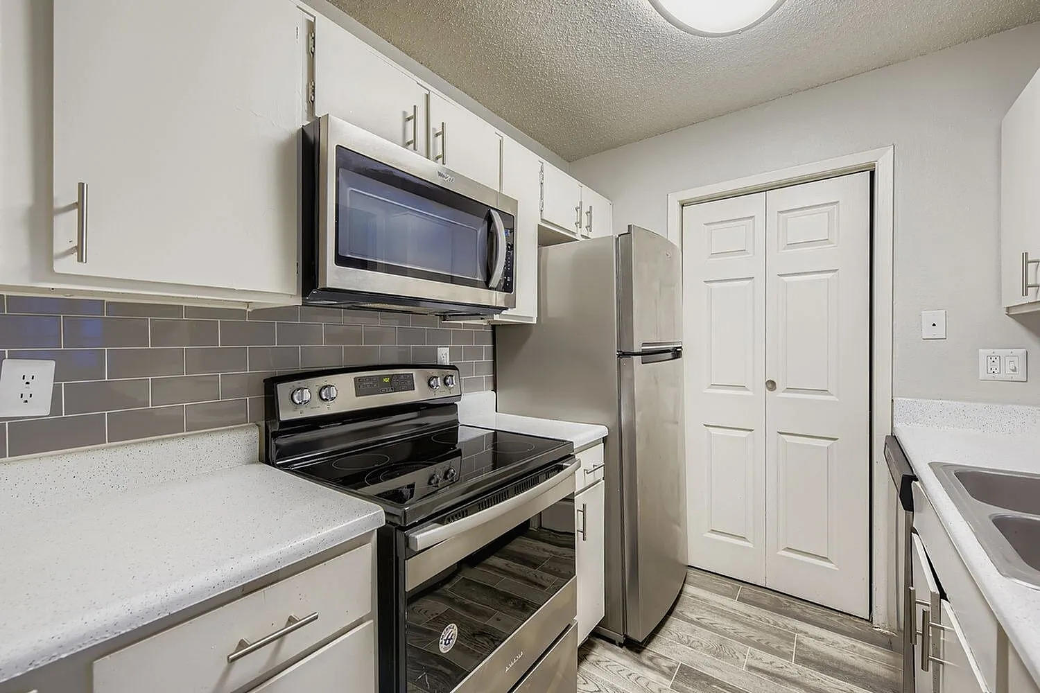 Kitchen, white shaker cabinetry, quartz countertops, stainless steel appliances, gray subway tile backsplash, wood-style plank flooring