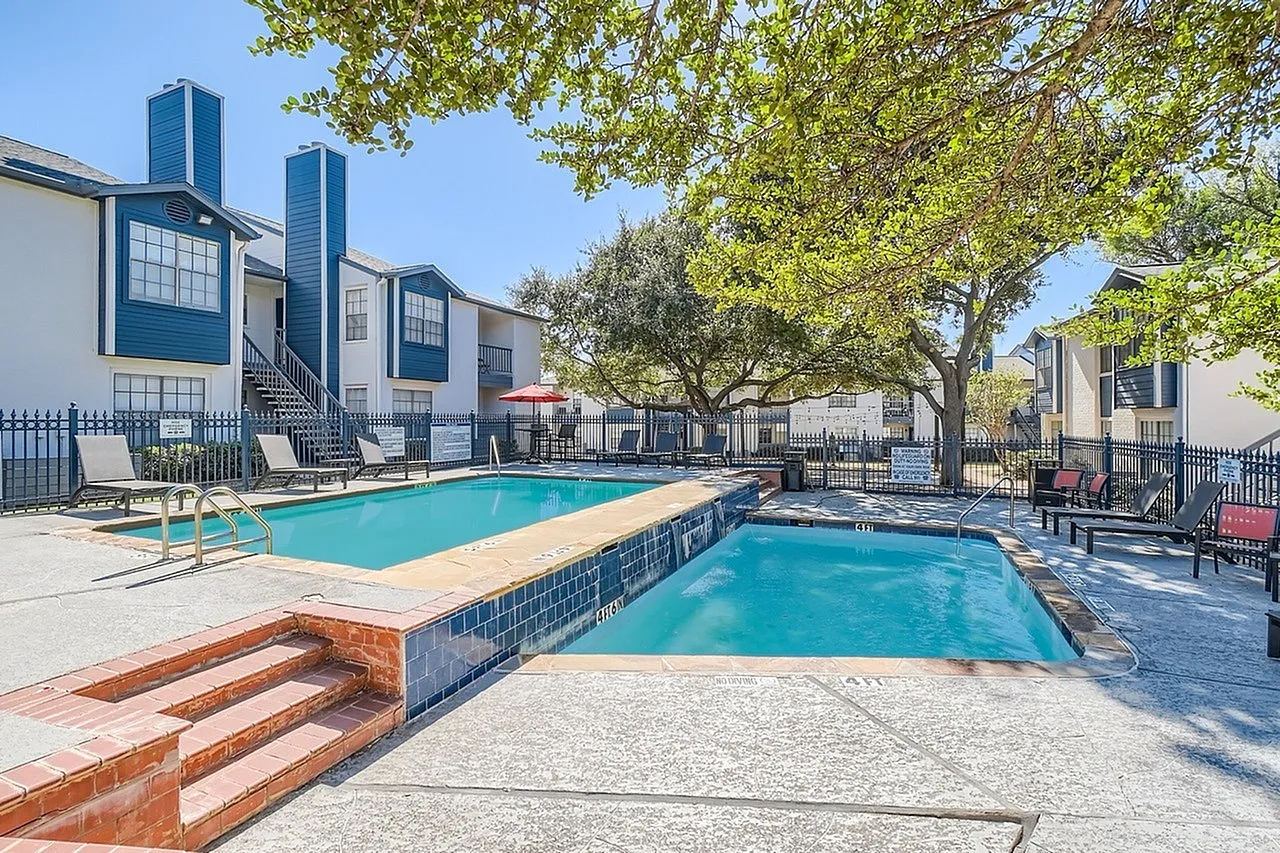 Swimming pool and spa, lounge chairs, apartment buildings, mature trees, clear blue sky