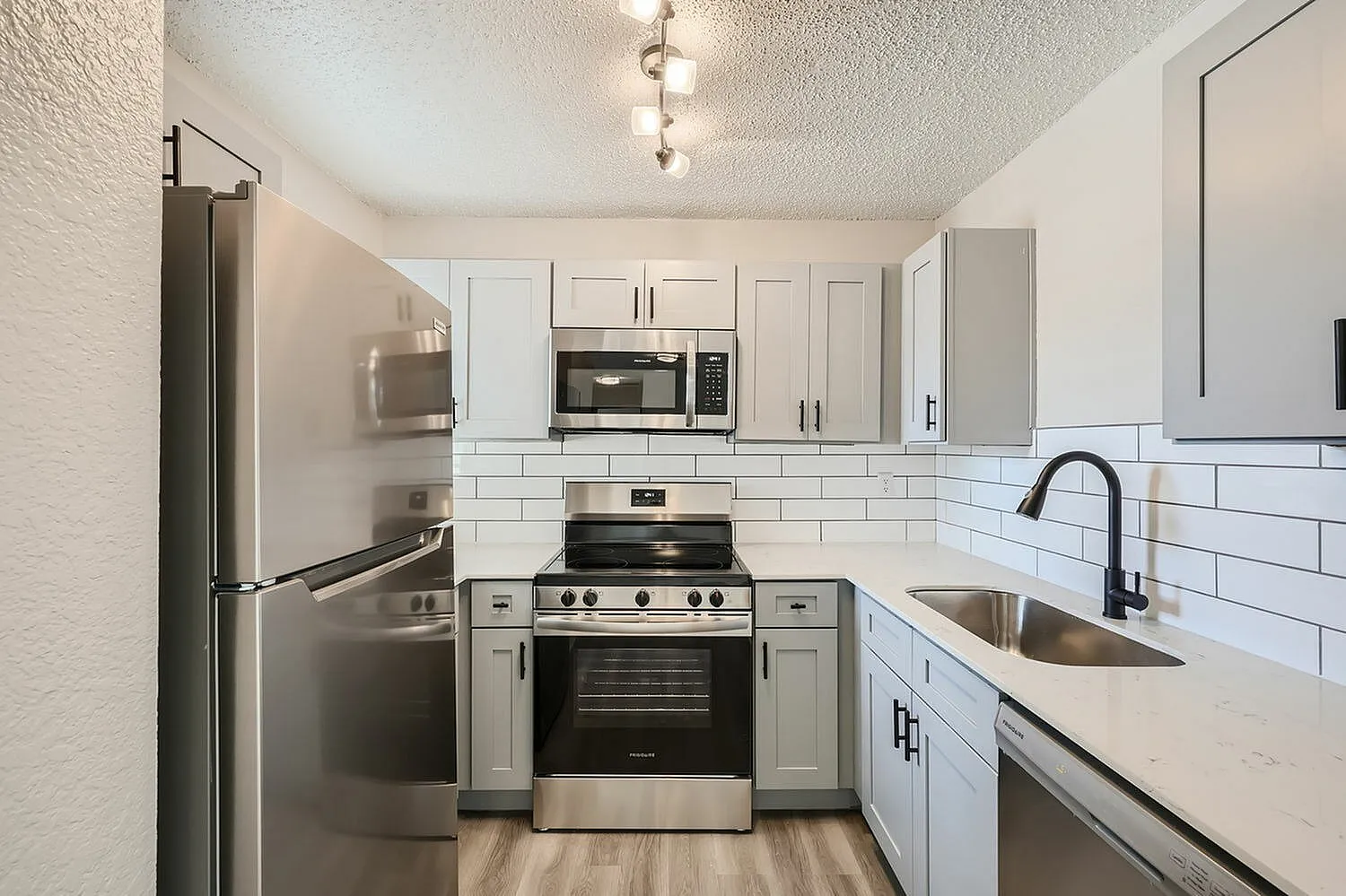 Kitchen, white shaker cabinetry, white subway tile backsplash, stainless appliances, wood-style plank flooring