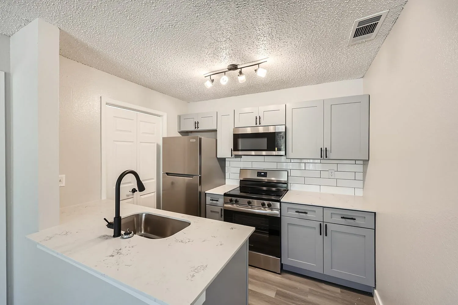Kitchen, white shaker cabinetry, quartz countertops, stainless appliances, wood-style plank flooring