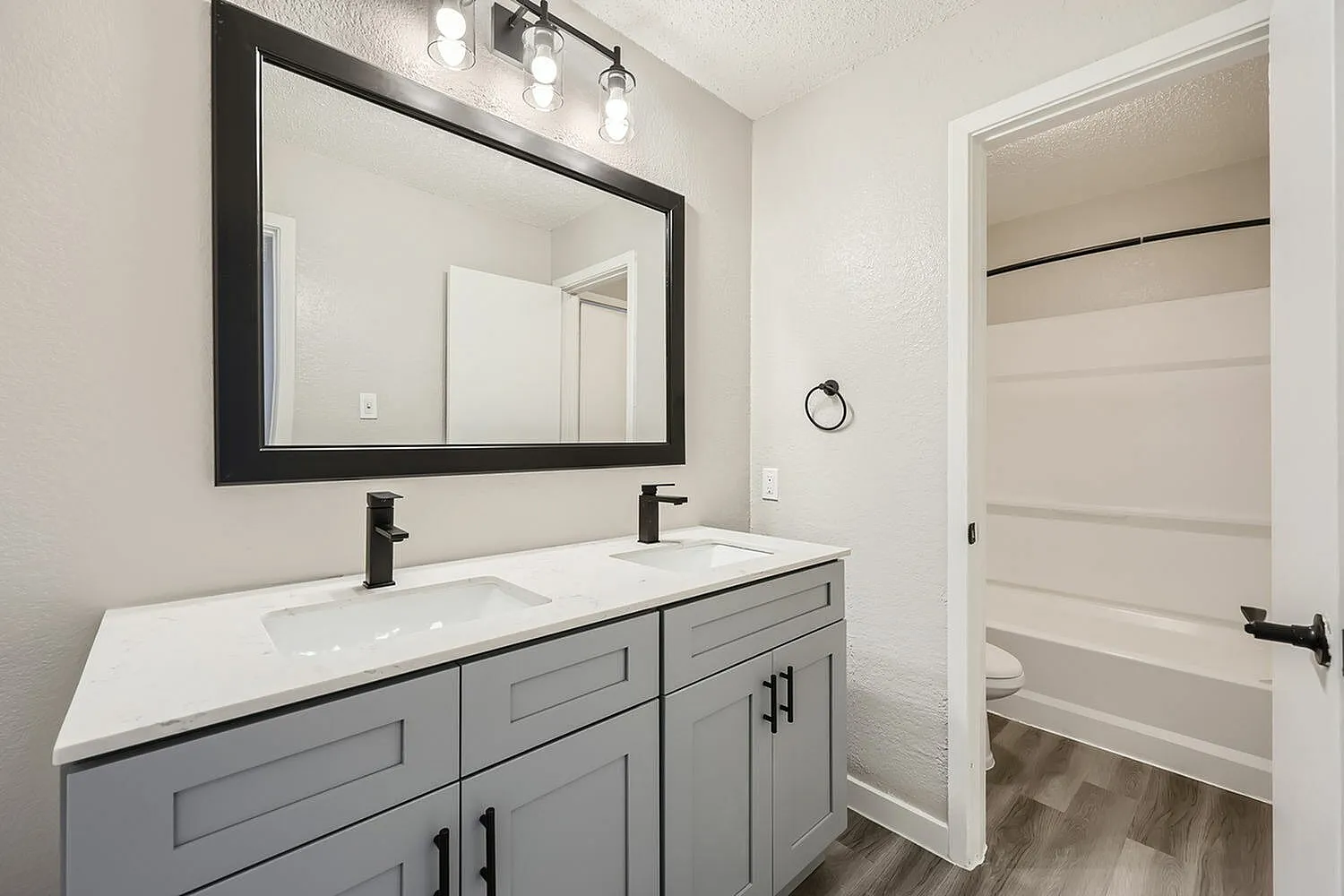 Primary bathroom, gray cabinetry, white countertop, black-framed mirror, black faucets
