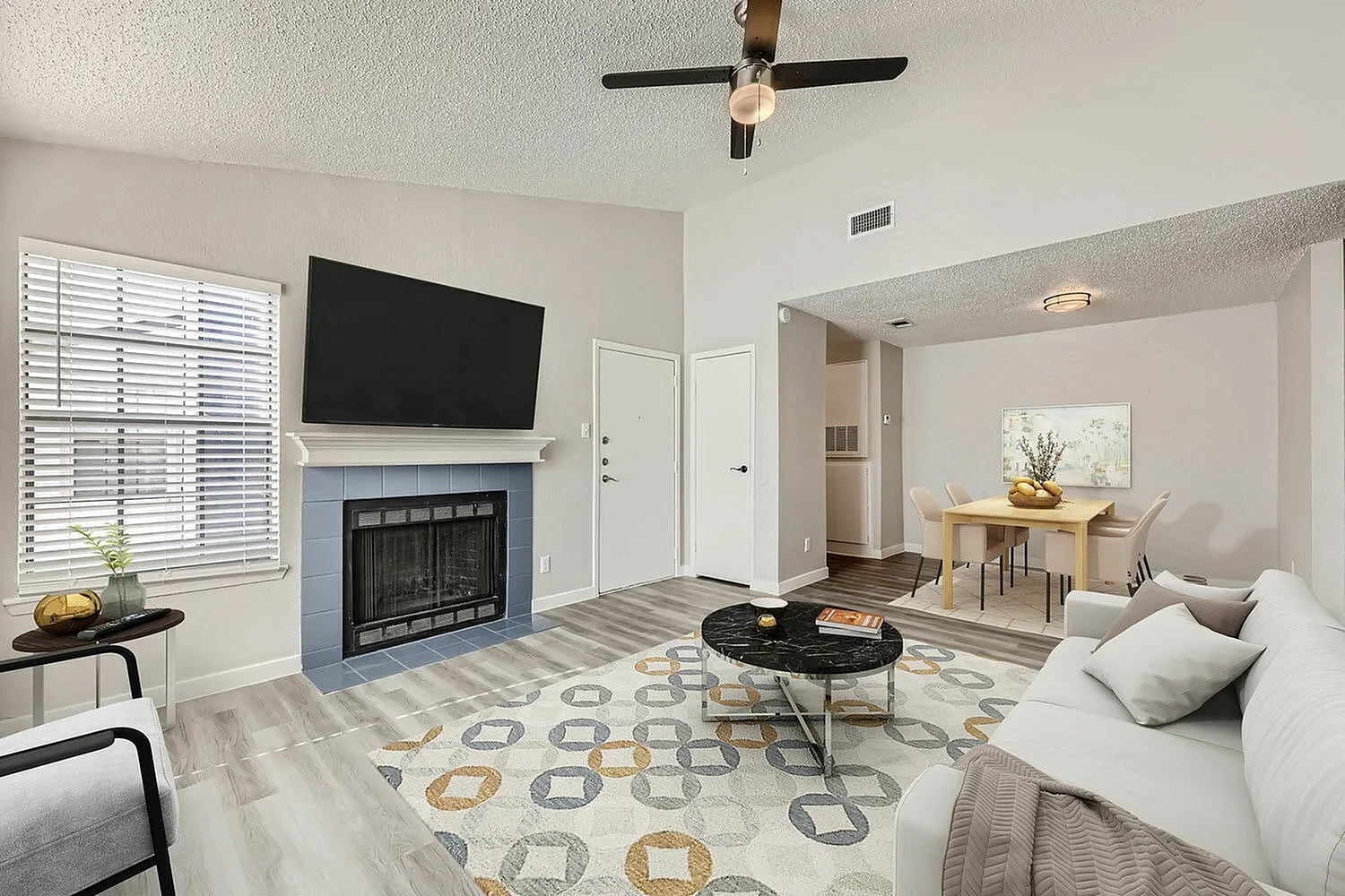 Living room, wood-style plank flooring, fireplace with TV, ceiling fan, patterned area rug