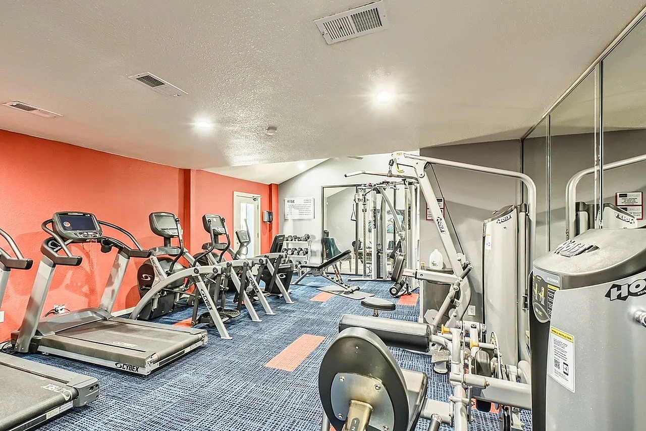 Fitness center, treadmills, stationary bikes, weight machines, blue carpet flooring, orange accent wall