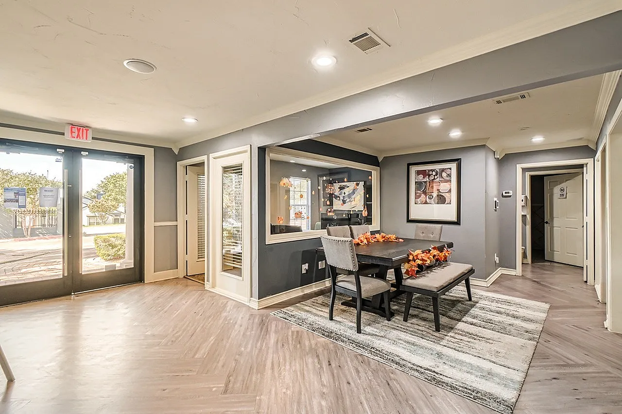 Dining area with black dining table, wood-style plank flooring, area rug, black accent wall with artwork