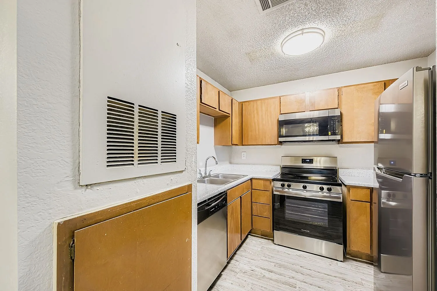 Kitchen, wood cabinetry, stainless steel appliances, white countertops, wood-style plank flooring