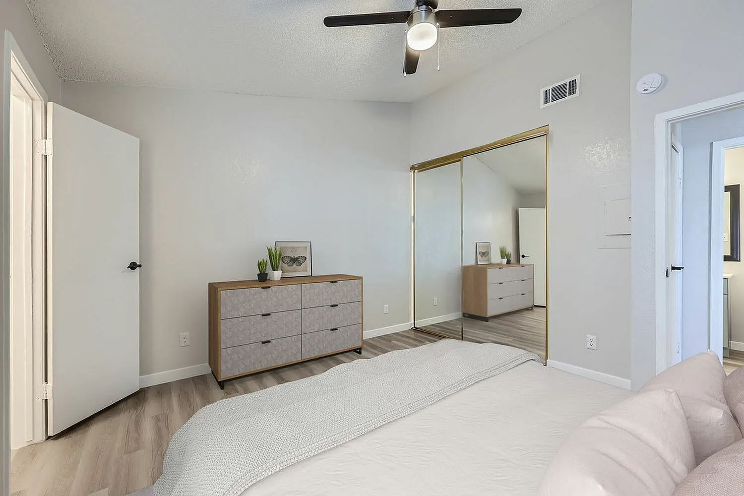 Primary bedroom, wood-style plank flooring, gray dresser, mirrored closet doors, ceiling fan