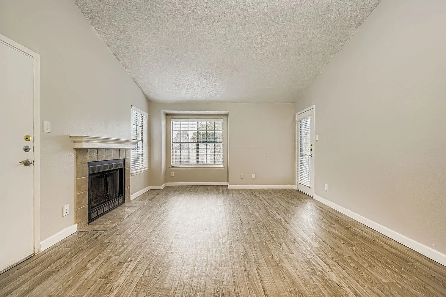 Living room, wood-style plank flooring, fireplace with stone surround, large bay window, shuttered door
