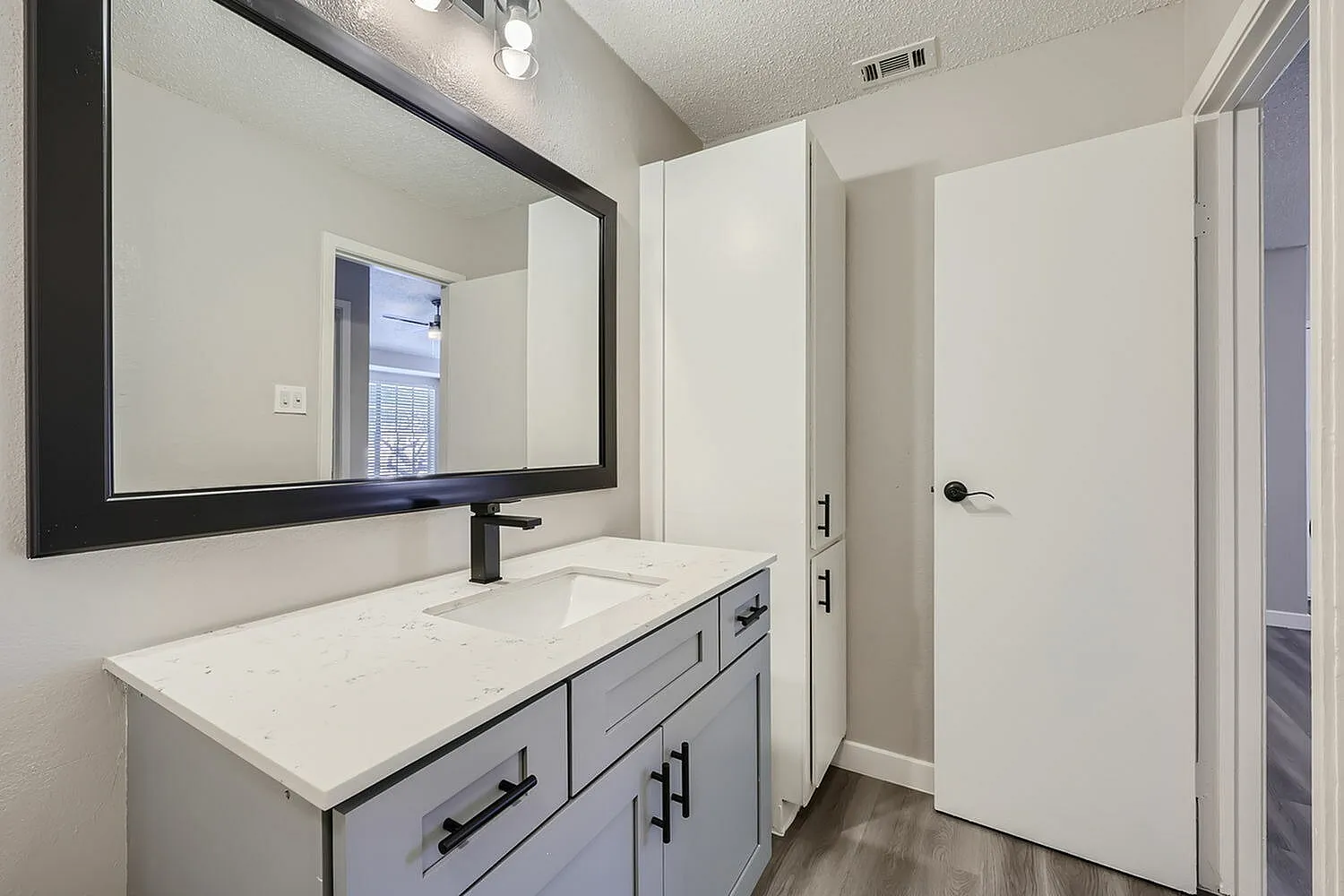 Primary bathroom, gray vanity with drawers, white quartz countertop, framed mirror, wood-style plank flooring