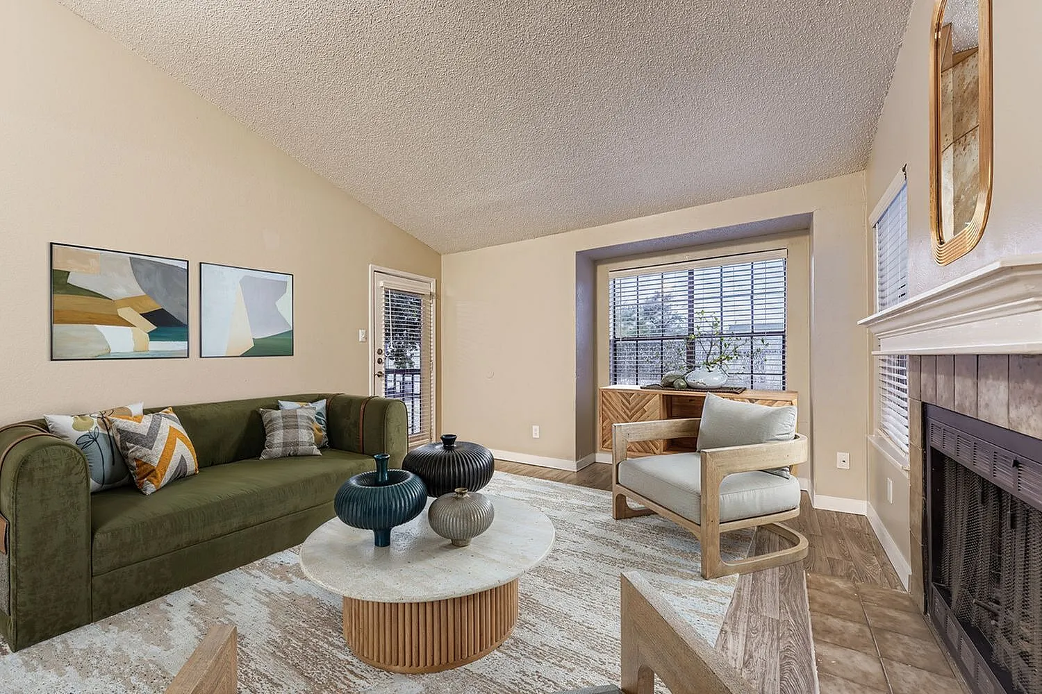 Living room, green upholstered sofa, wood-style plank flooring, fireplace, large windows