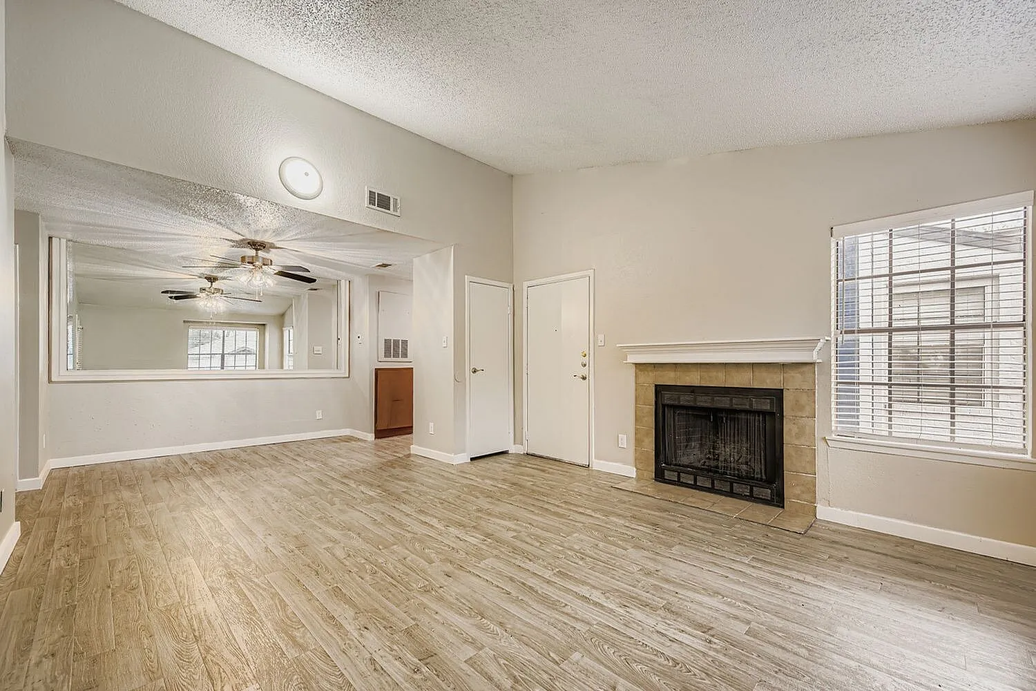 Living room, wood-style plank flooring, fireplace, ceiling fan, large mirror
