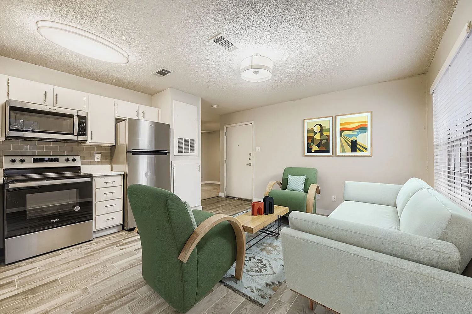 Open kitchen and living room, white cabinetry, stainless appliances, wood-style plank flooring, green accent chairs