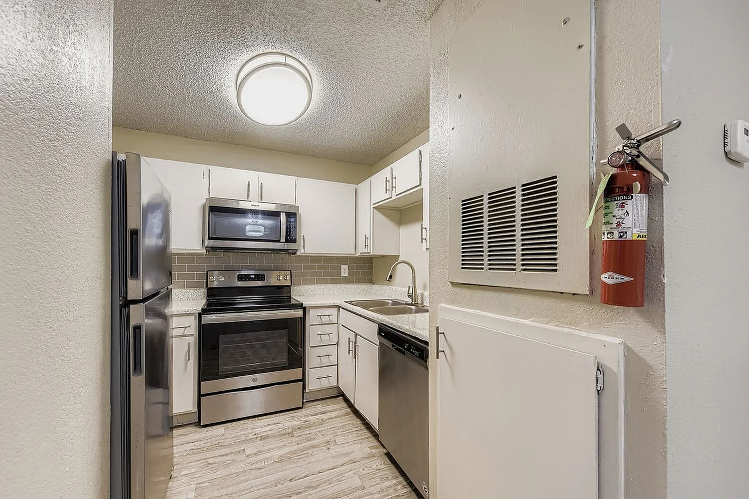 Kitchen, white shaker cabinetry, stainless steel appliances, wood-style plank flooring, tile backsplash