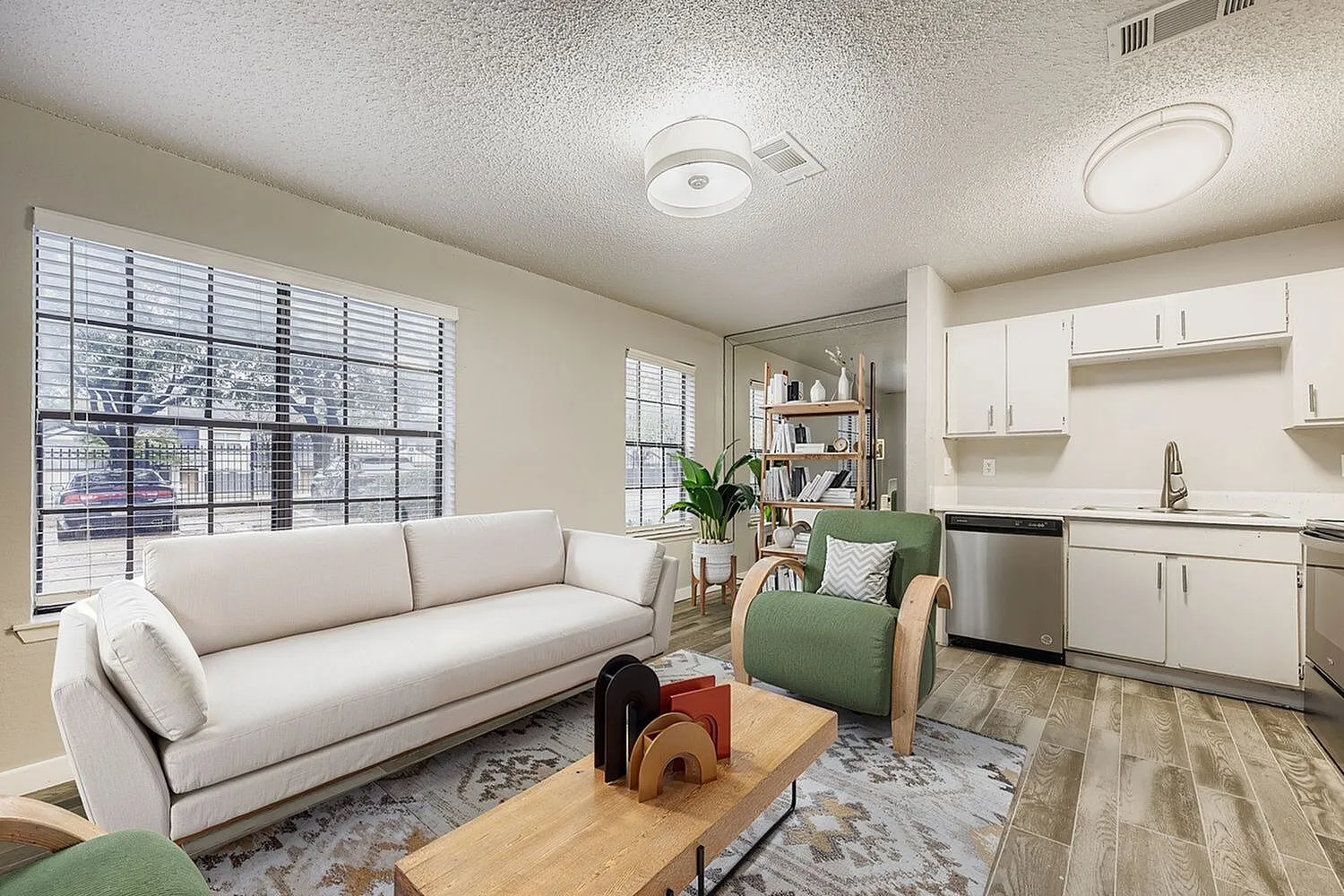 Open living room and kitchen, white cabinetry, stainless appliances, wood-style plank flooring, large windows