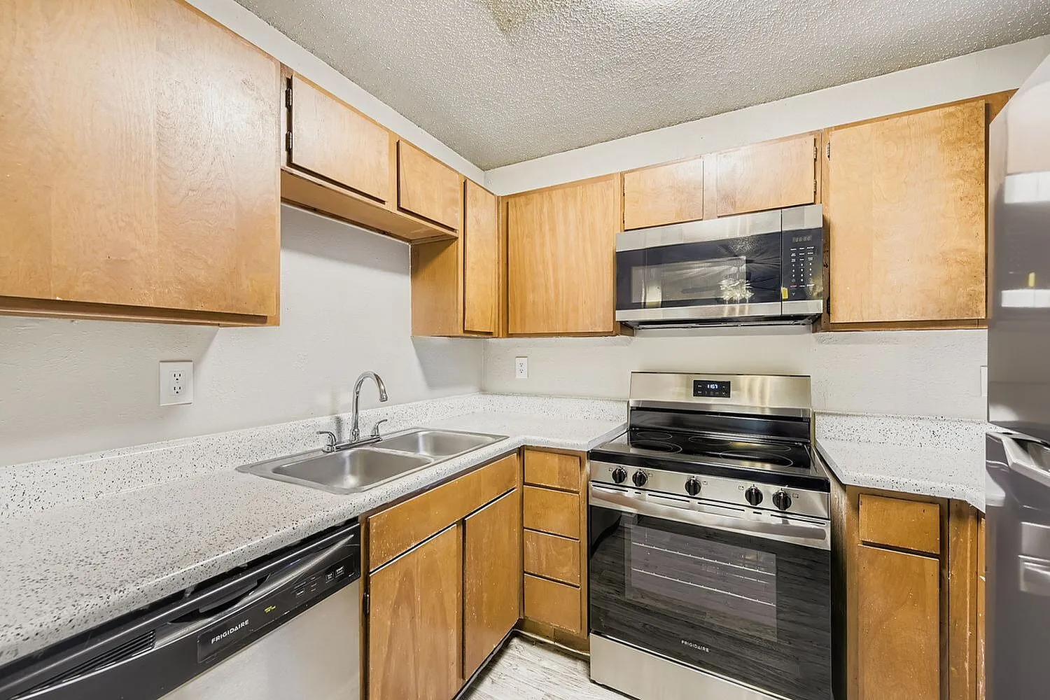 Kitchen, wood cabinetry, speckled countertops, stainless appliances, microwave