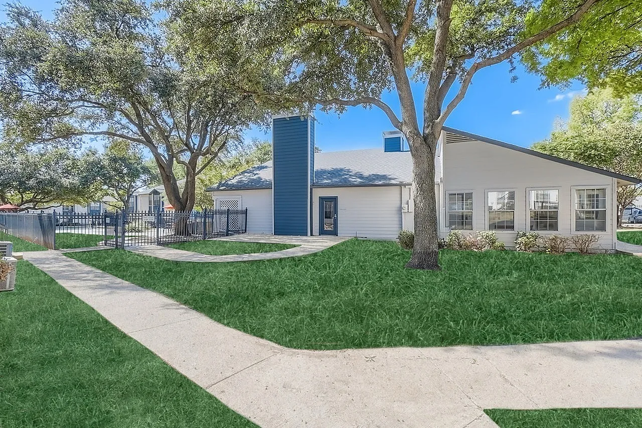 Modern white building with dark blue accent tower, large windows, mature trees, manicured lawn