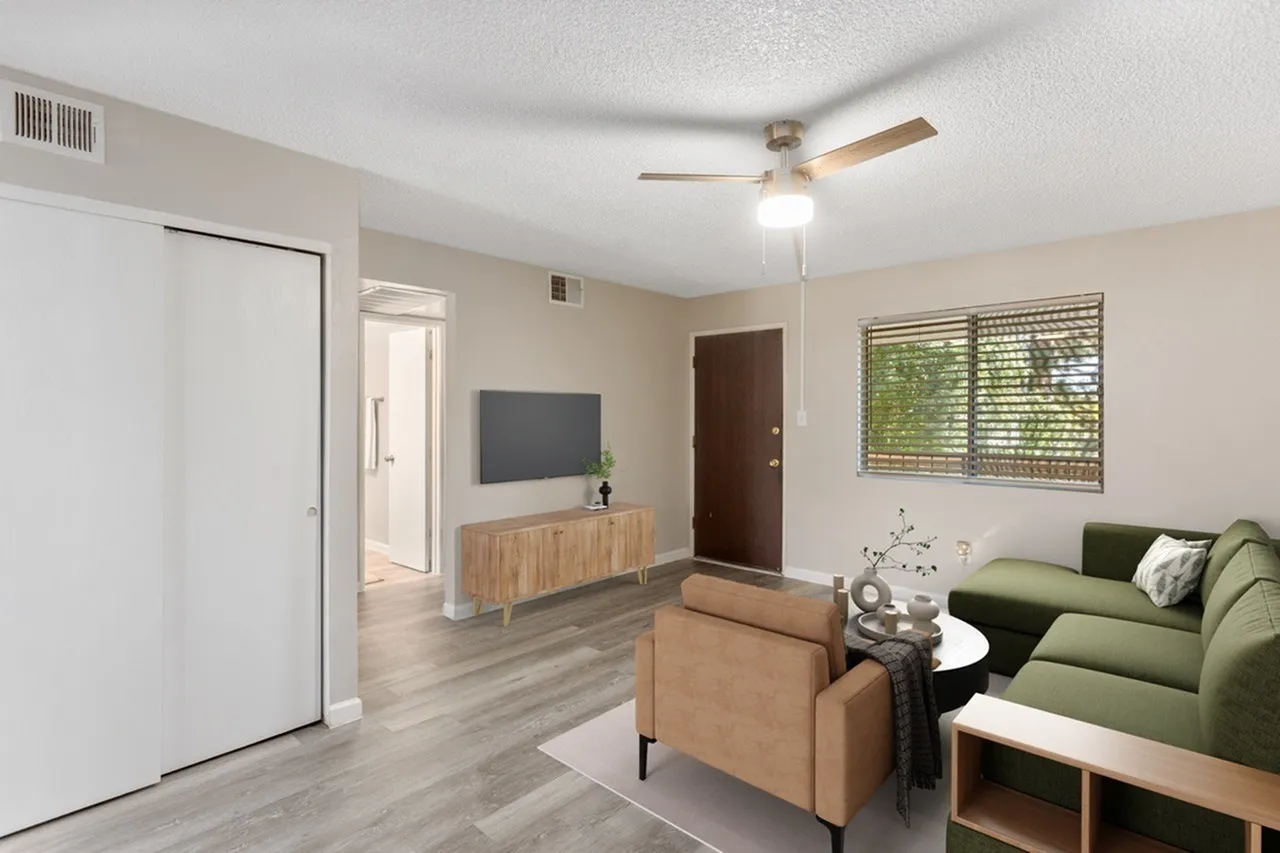 Living room with wood-style plank flooring, green sofa, ceiling fan, TV on media console