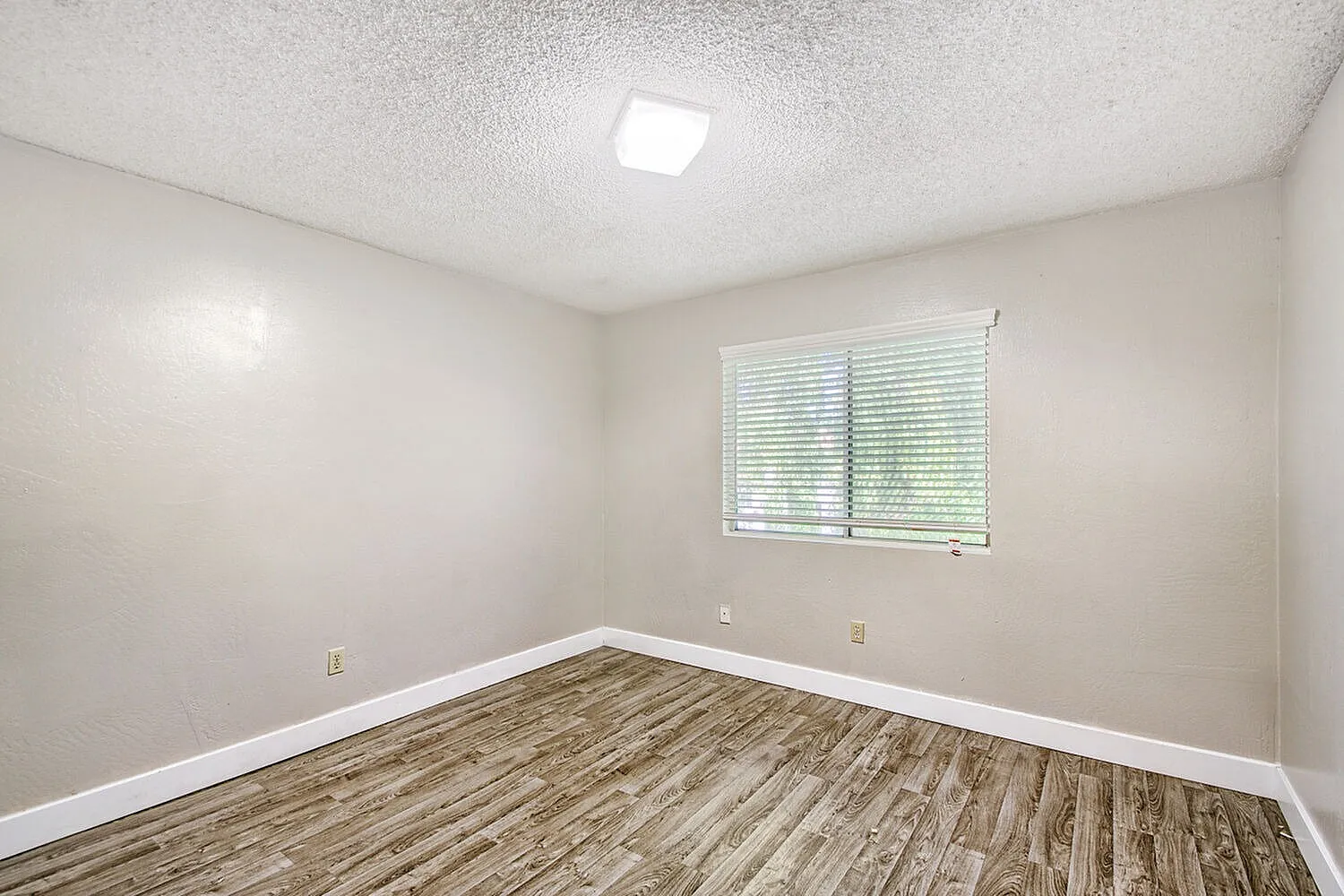 Bedroom, wood-style plank flooring, white base trim, recessed ceiling light, window with blinds