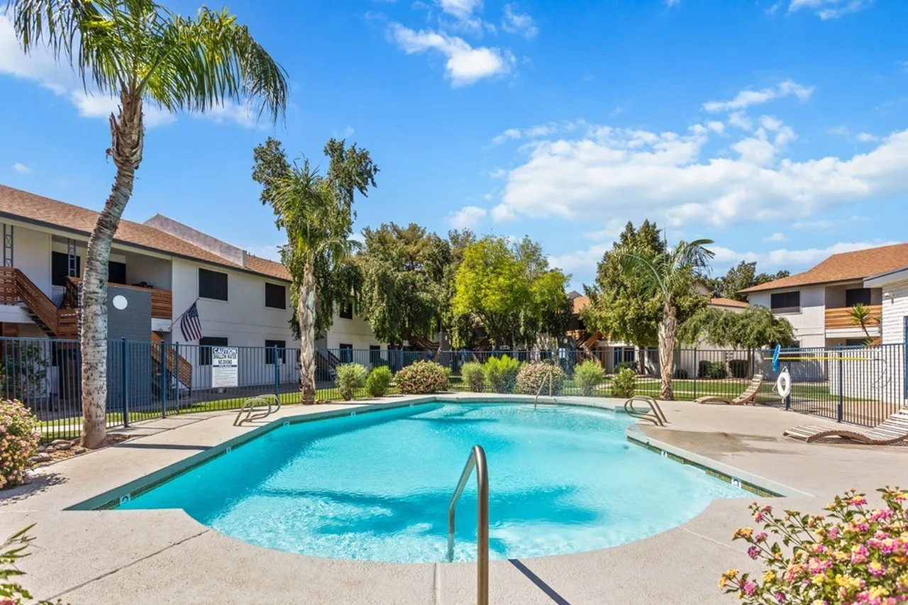 Resort-style pool, surrounding patio, palm trees, blue sky, residential buildings