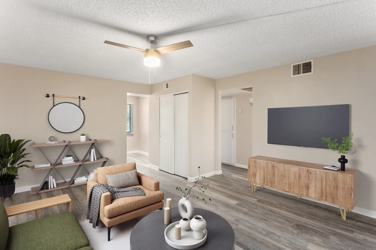 Living room with wood-style plank flooring, tan leather armchair, ceiling fan, wall-mounted TV, round coffee table