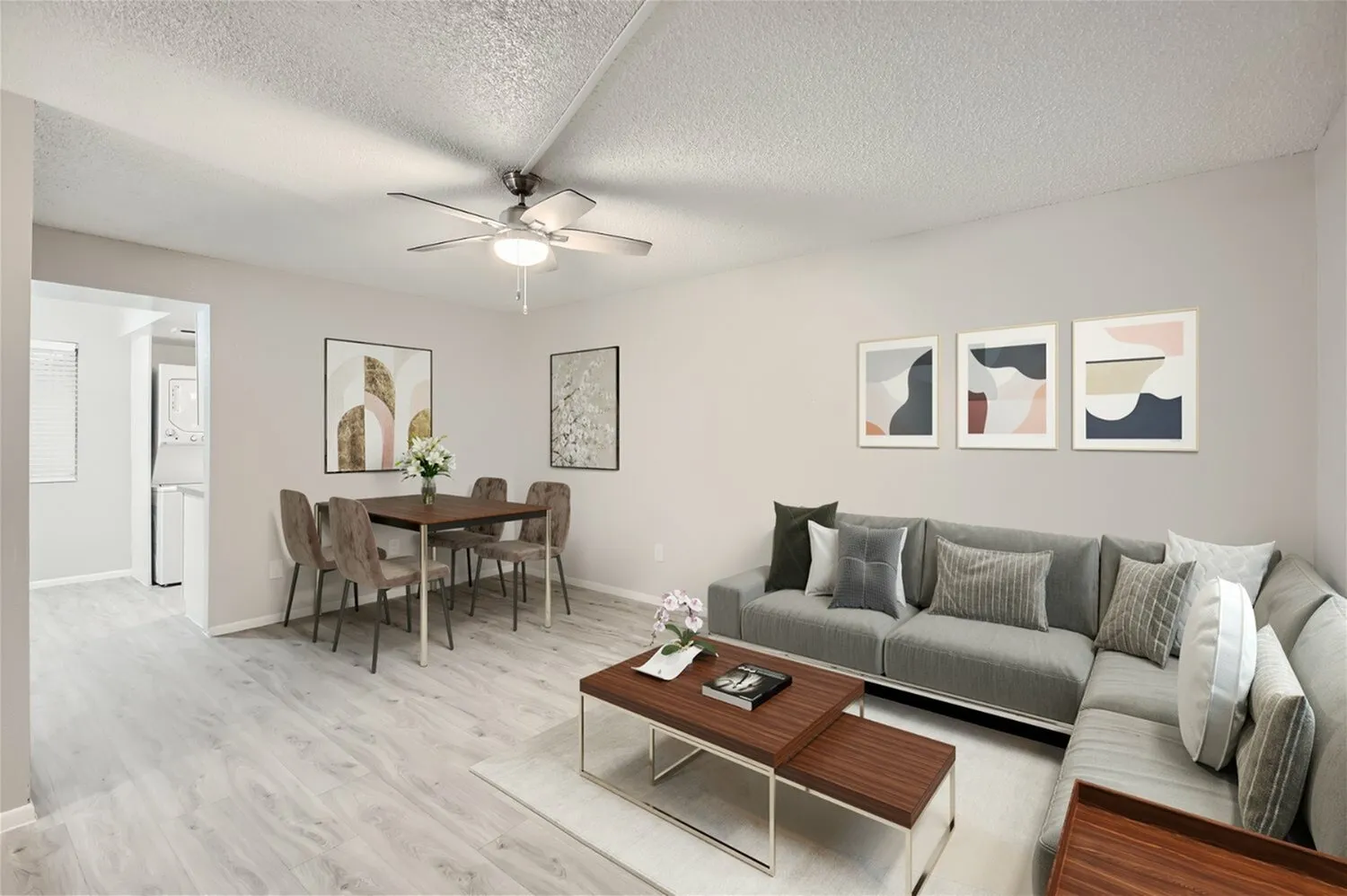 Living room with wood-style plank flooring, gray sofa, ceiling fan, dining table