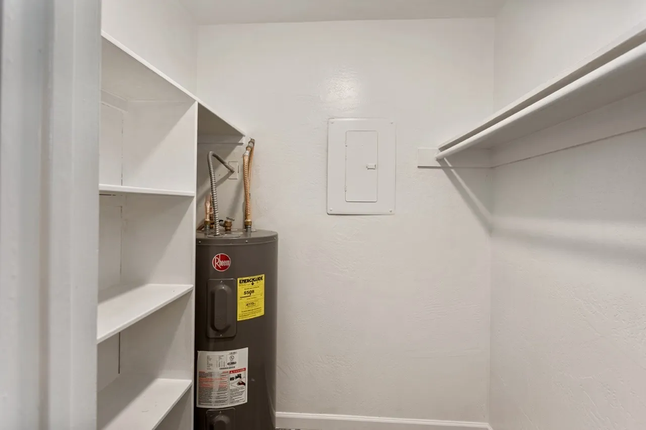 Laundry room, white shelving, water heater, light switch, rod for hanging