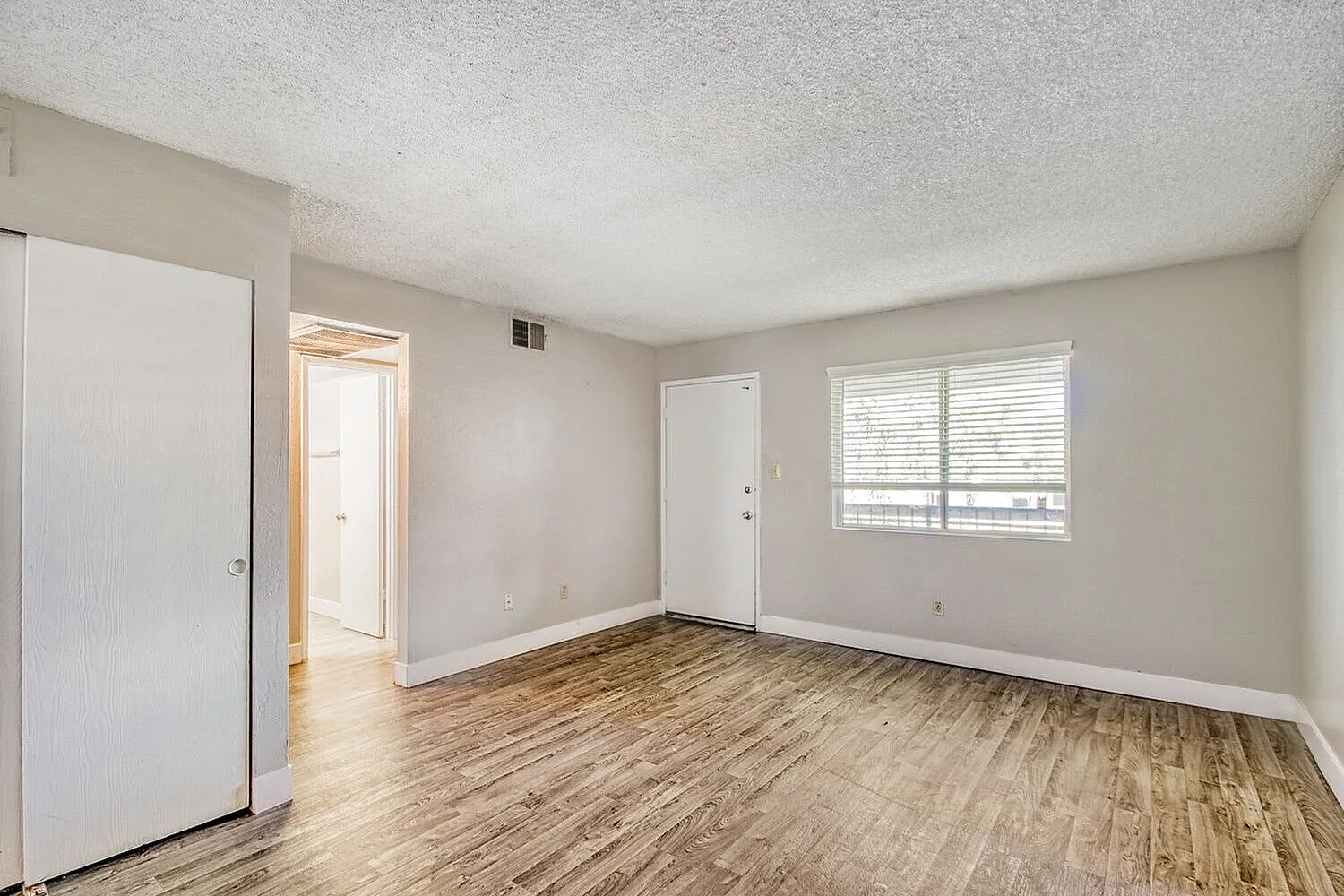 Bedroom with wood-style plank flooring, white closet door, large window with blinds