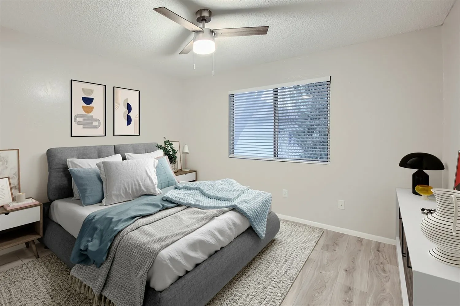 Primary bedroom, gray upholstered bed, wood-style plank flooring, ceiling fan with light fixture