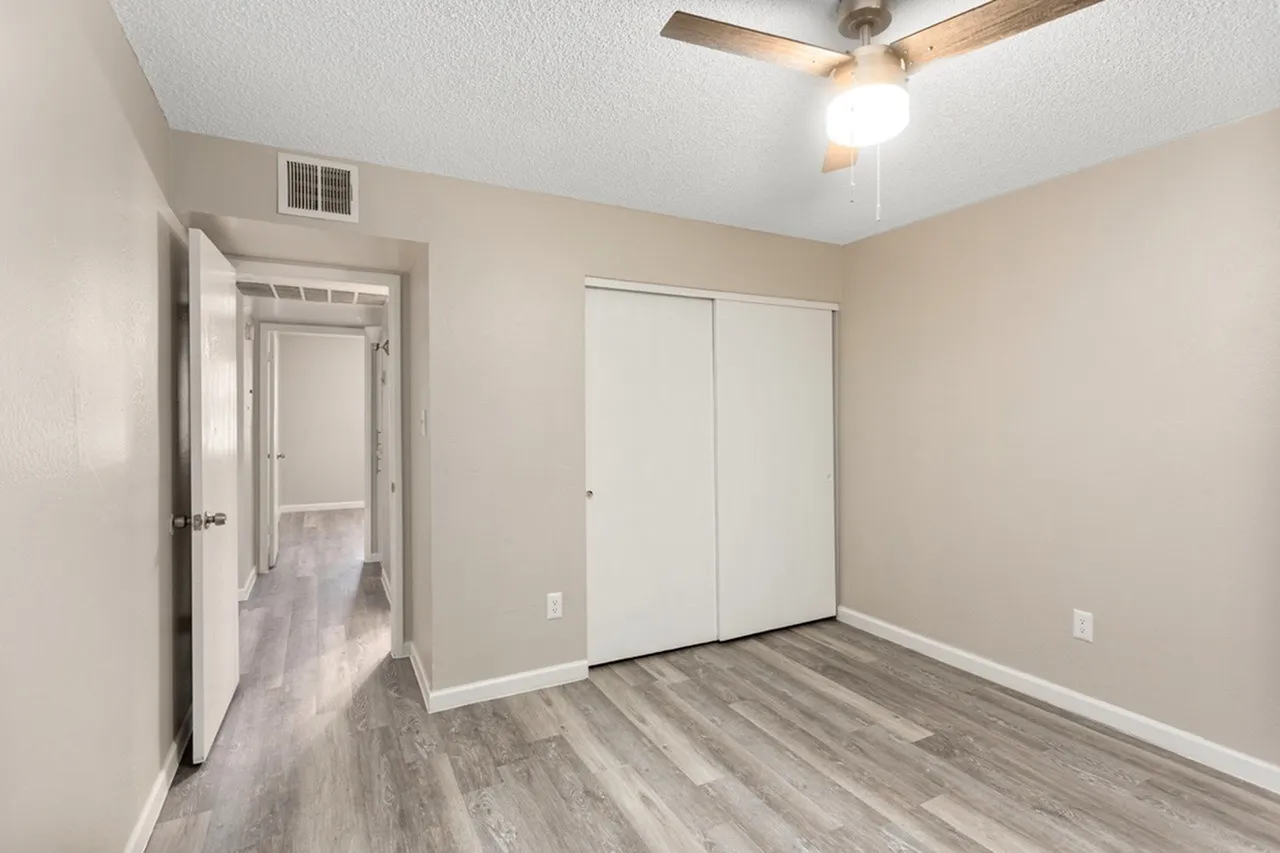 Primary bedroom, wood-style plank flooring, ceiling fan, closet doors, neutral walls