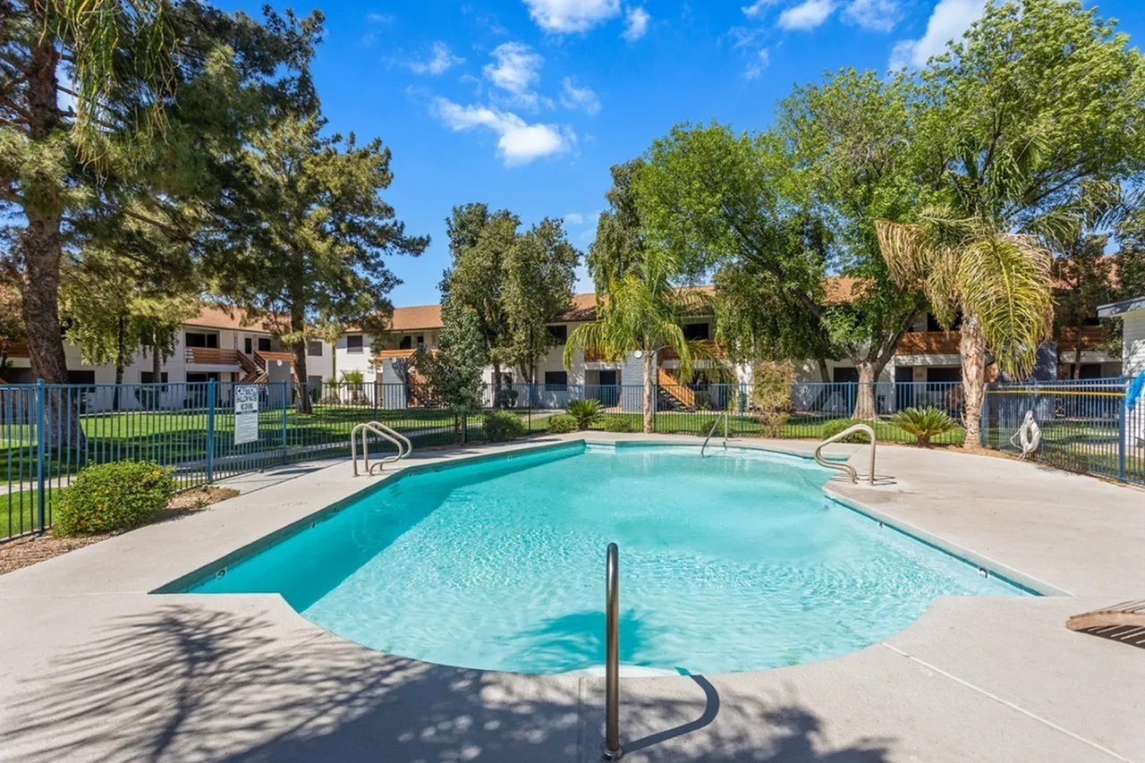 Resort pool with turquoise water, black safety rail, concrete deck, palm trees, residential buildings