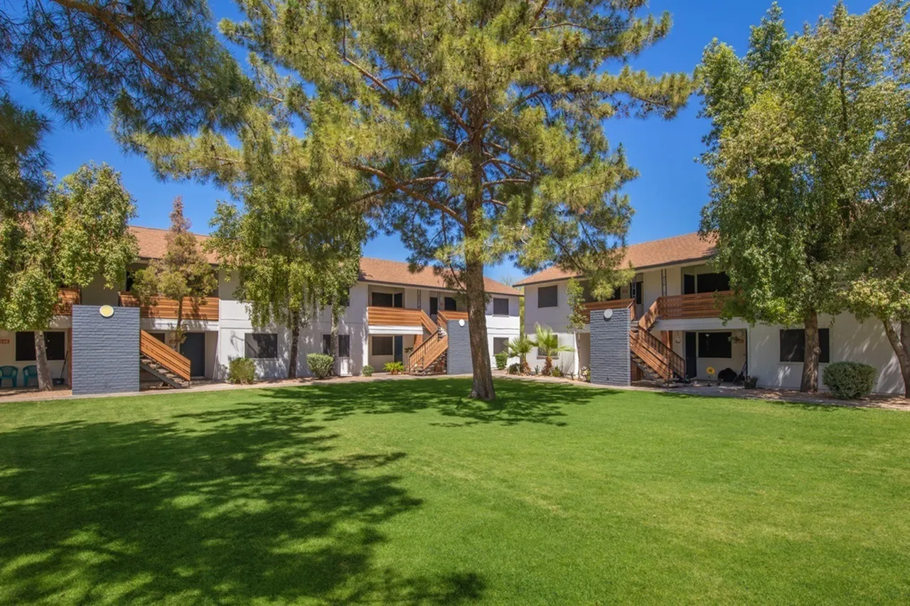 Courtyard with large shade trees, green lawn, multi-story residential buildings, clear blue sky